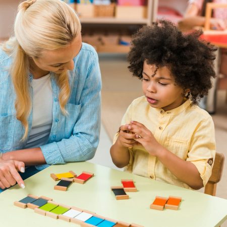 African american child playing educational game by teacher at table in montessori class