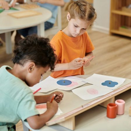 multiethnic children drawing with pencils on table in class of montessori school