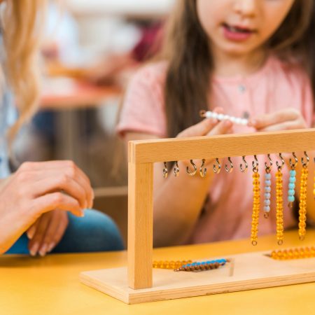 Selective focus of kid playing wooden game by teacher in montessori school, cropped view