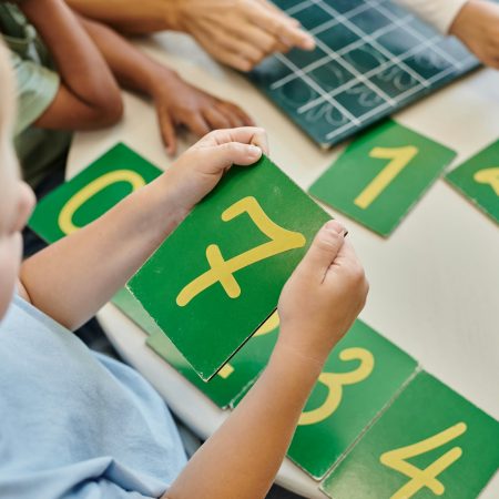 top view of boy holding number seven card, learning how to count in Montessori school, study